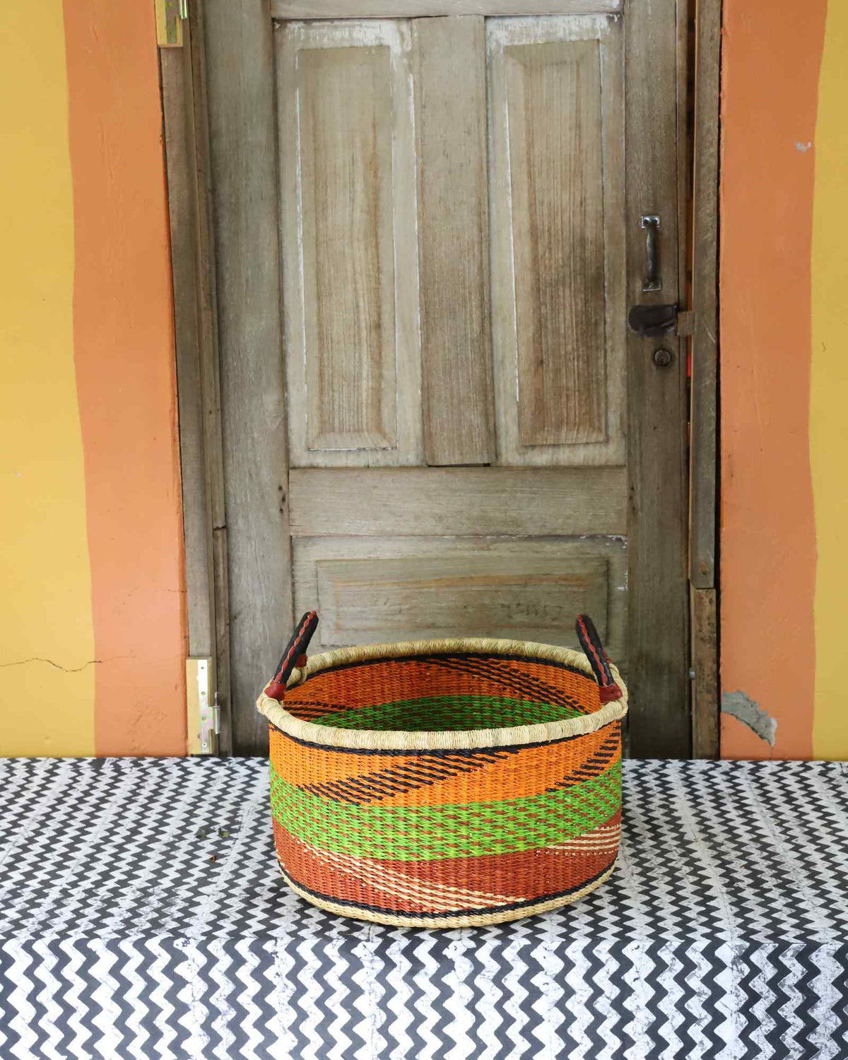 Small handwoven Bolga storage tub in natural straw with fine orange and green banded stripes.