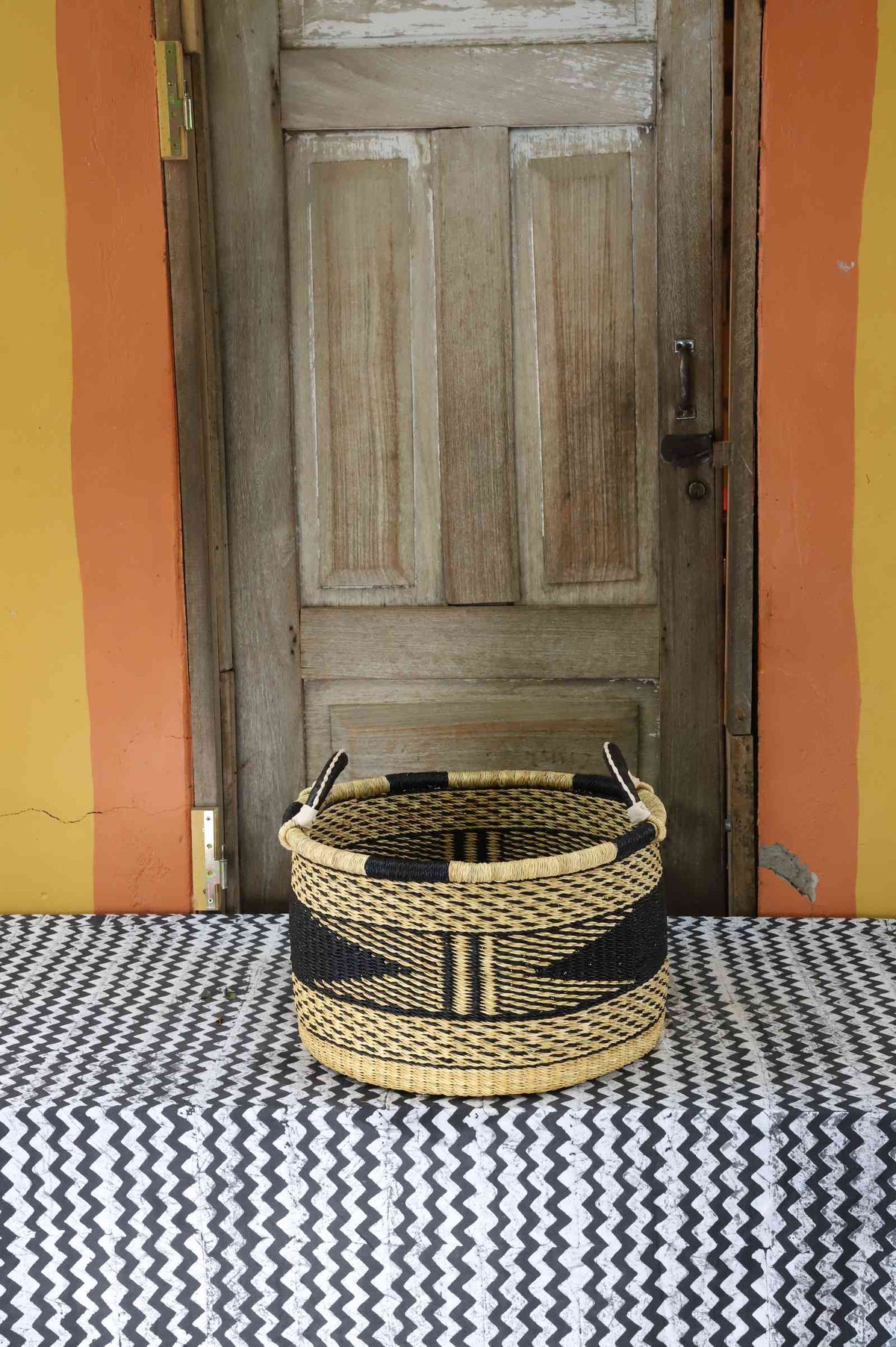 Small handwoven Bolga storage tub in dyed black with fine natural stripes and leather-wrapped handles.