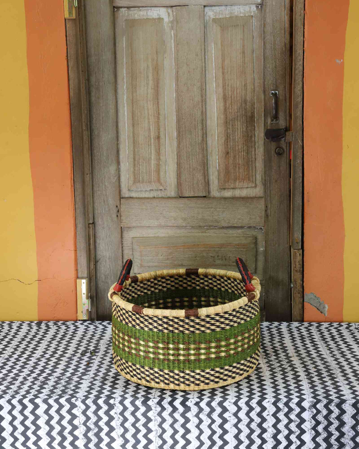 Small handwoven Bolga storage tub in dyed dark green with fine stripes and dark leather handles.