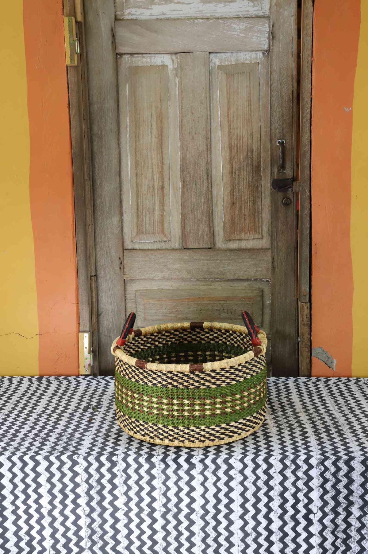 Small handwoven Bolga storage tub in dyed dark green with fine stripes and dark leather handles.