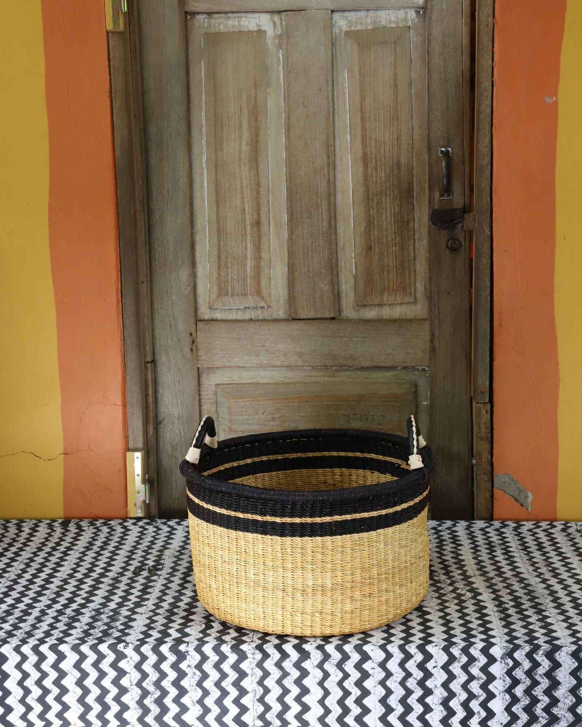 Small handwoven Bolga storage tub in natural straw with a plain body and dark banded rim.