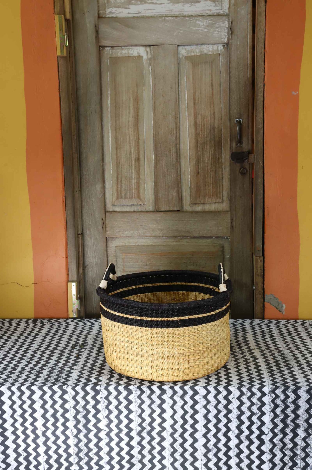 Small handwoven Bolga storage tub in natural straw with a plain body and dark banded rim.