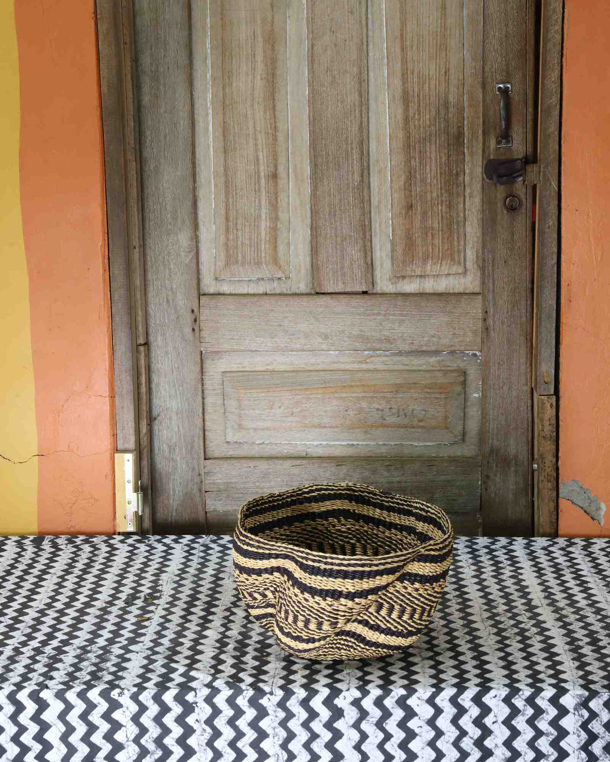 Tiny handwoven Bolga wave basket in natural straw with black horizontal wave stripes.