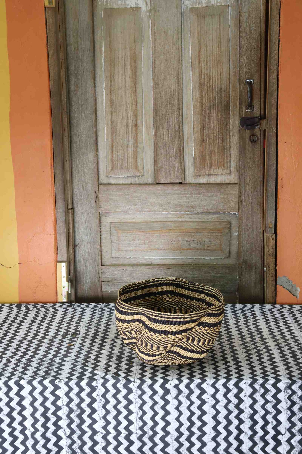 Tiny handwoven Bolga wave basket in natural straw with black horizontal wave stripes.