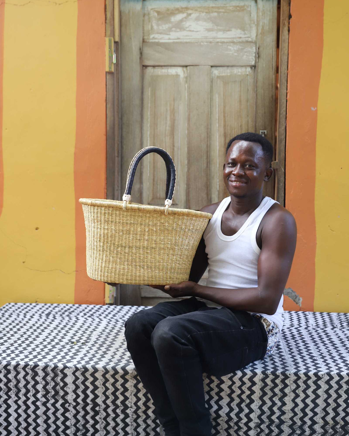 Medium Bolga Zaane Tia market basket in plain natural straw, held by a seated man in white.