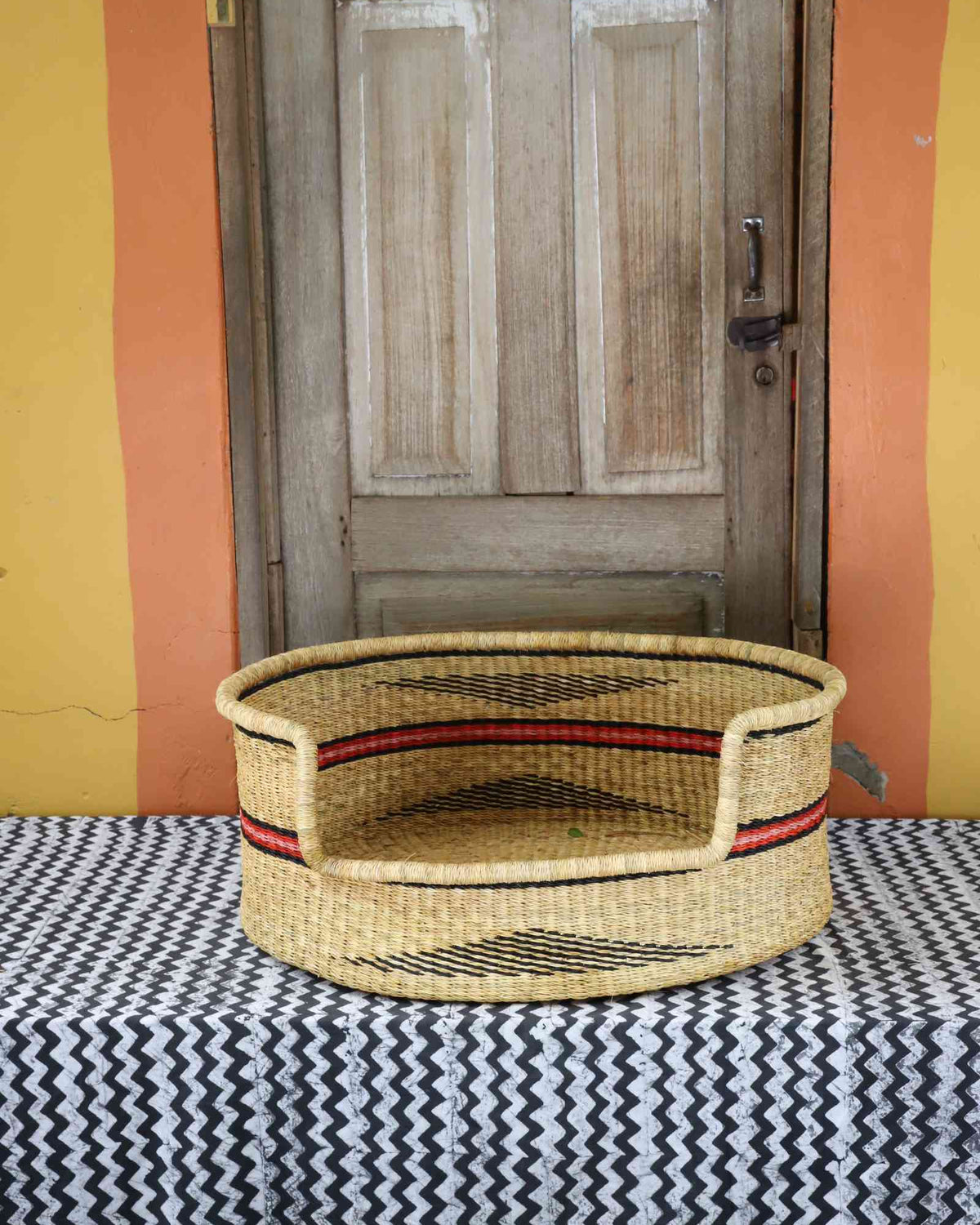 Large handwoven Bolga pet bed in natural straw with fine red horizontal stripes.