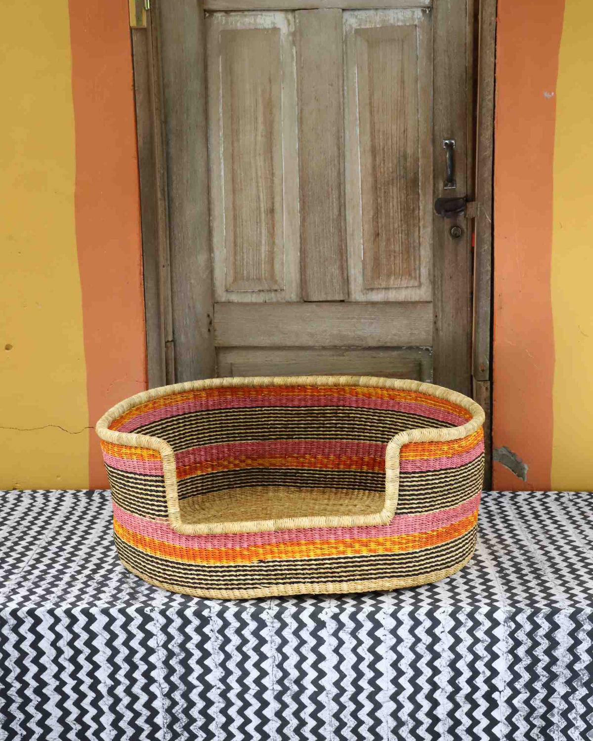 Large handwoven Bolga pet bed in natural straw with fine orange and red horizontal stripes.