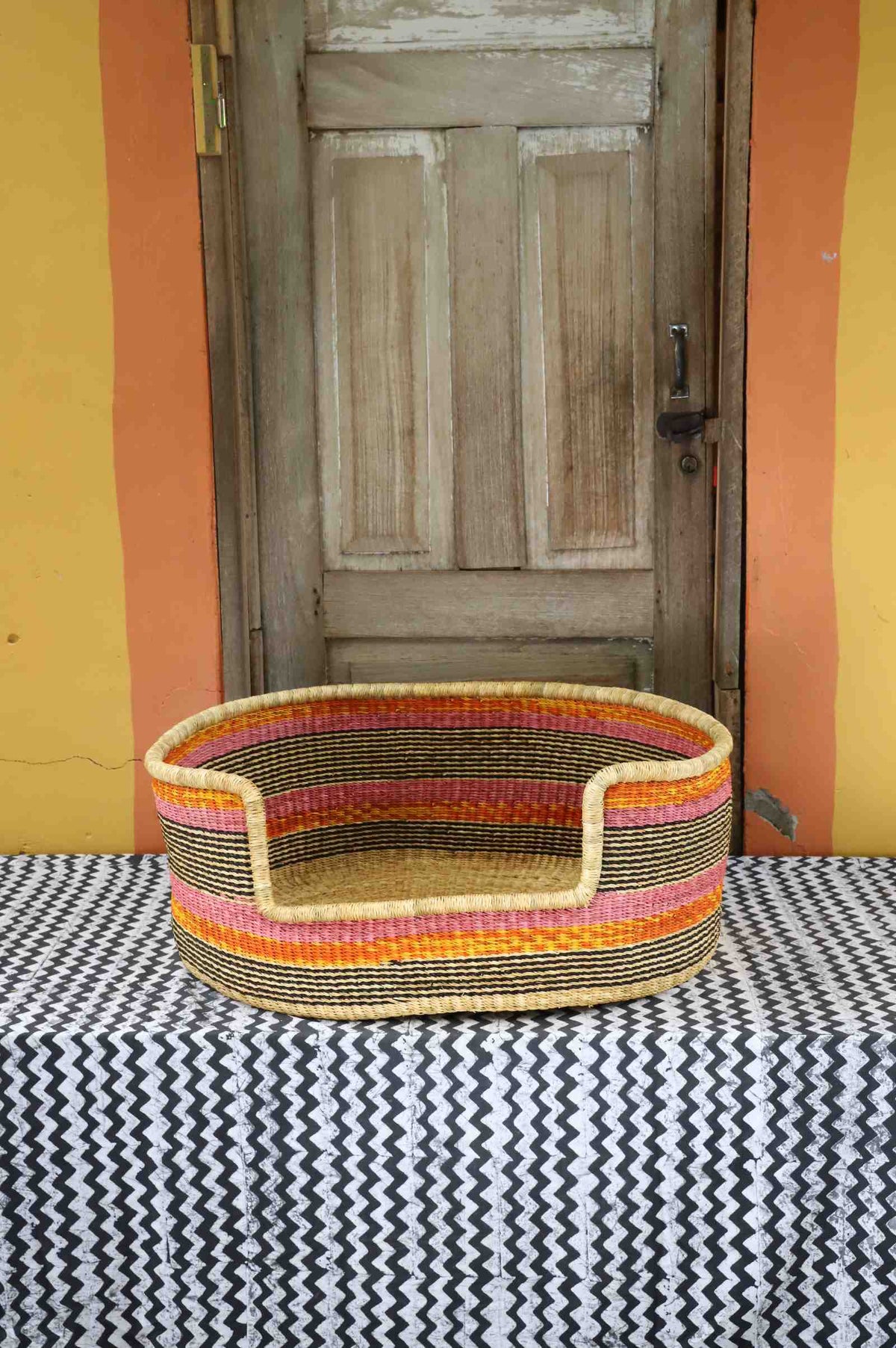 Large handwoven Bolga pet bed in natural straw with fine orange and red horizontal stripes.