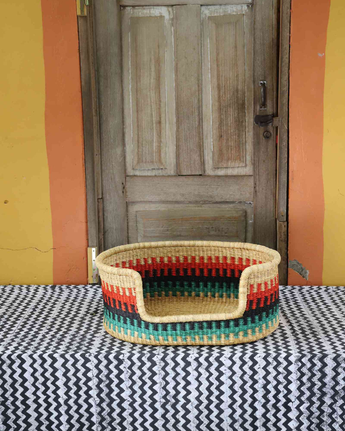Small handwoven Bolga pet bed in natural straw with red, green and yellow vertical stripes and a green rim.