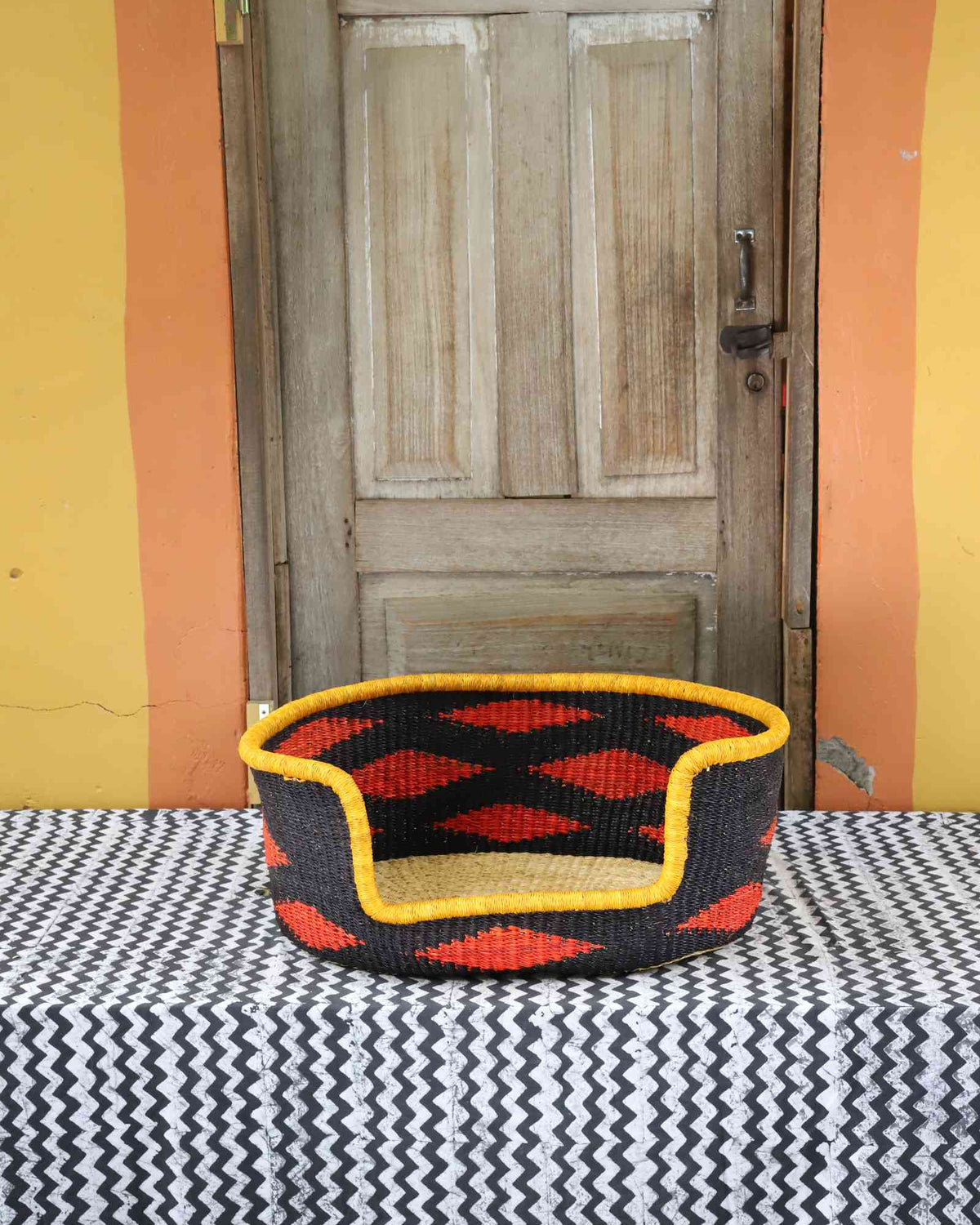 Small handwoven Bolga pet bed in bold black with orange diamond pattern and yellow rim.