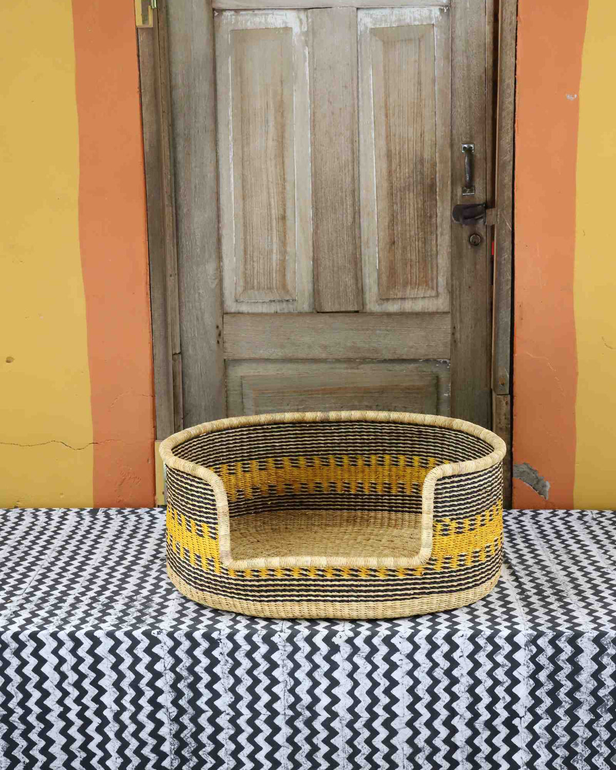 Medium handwoven Bolga pet bed in natural straw with fine yellow banded stripes and a dark rim.