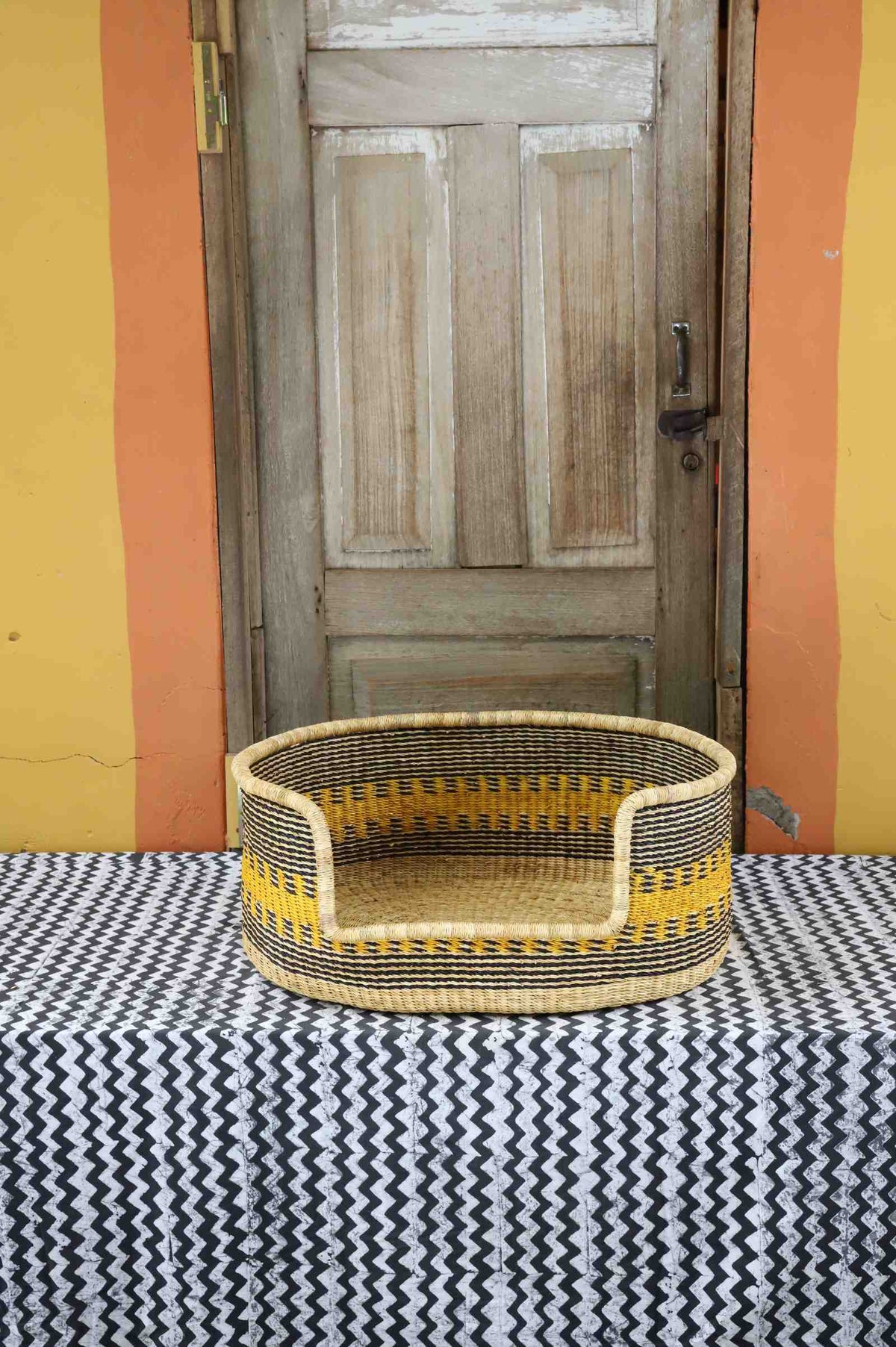 Medium handwoven Bolga pet bed in natural straw with fine yellow banded stripes and a dark rim.