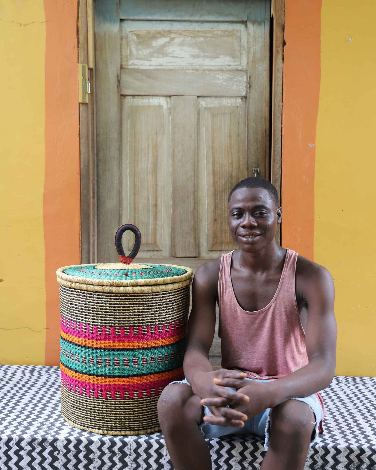 Handwoven Bolga laundry basket in fine multicolour stripes, styled beside a seated man in pink.