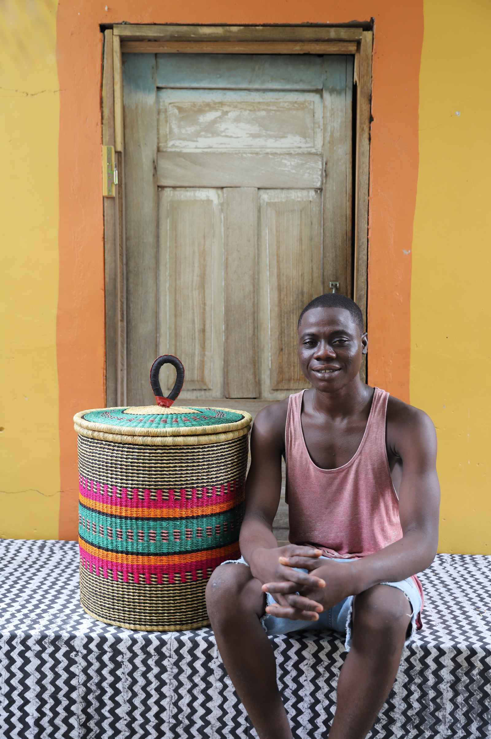 Handwoven Bolga laundry basket in fine multicolour stripes, styled beside a seated man in pink.
