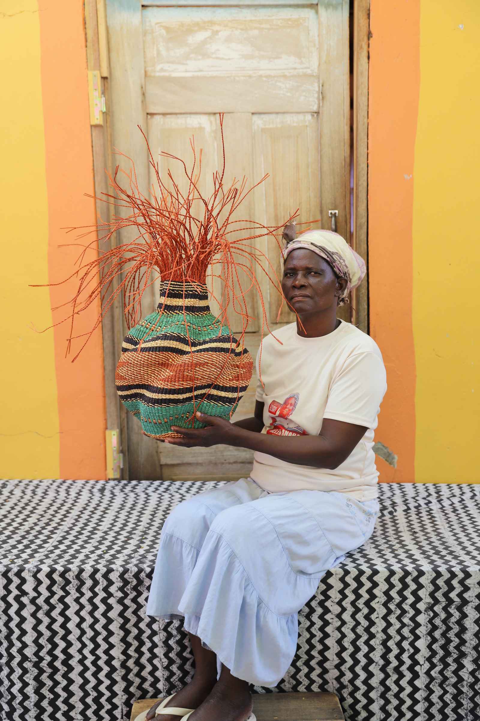 Handwoven Bolga Baobab basket with orange and teal wave bands, held by a seated woman in a white top.