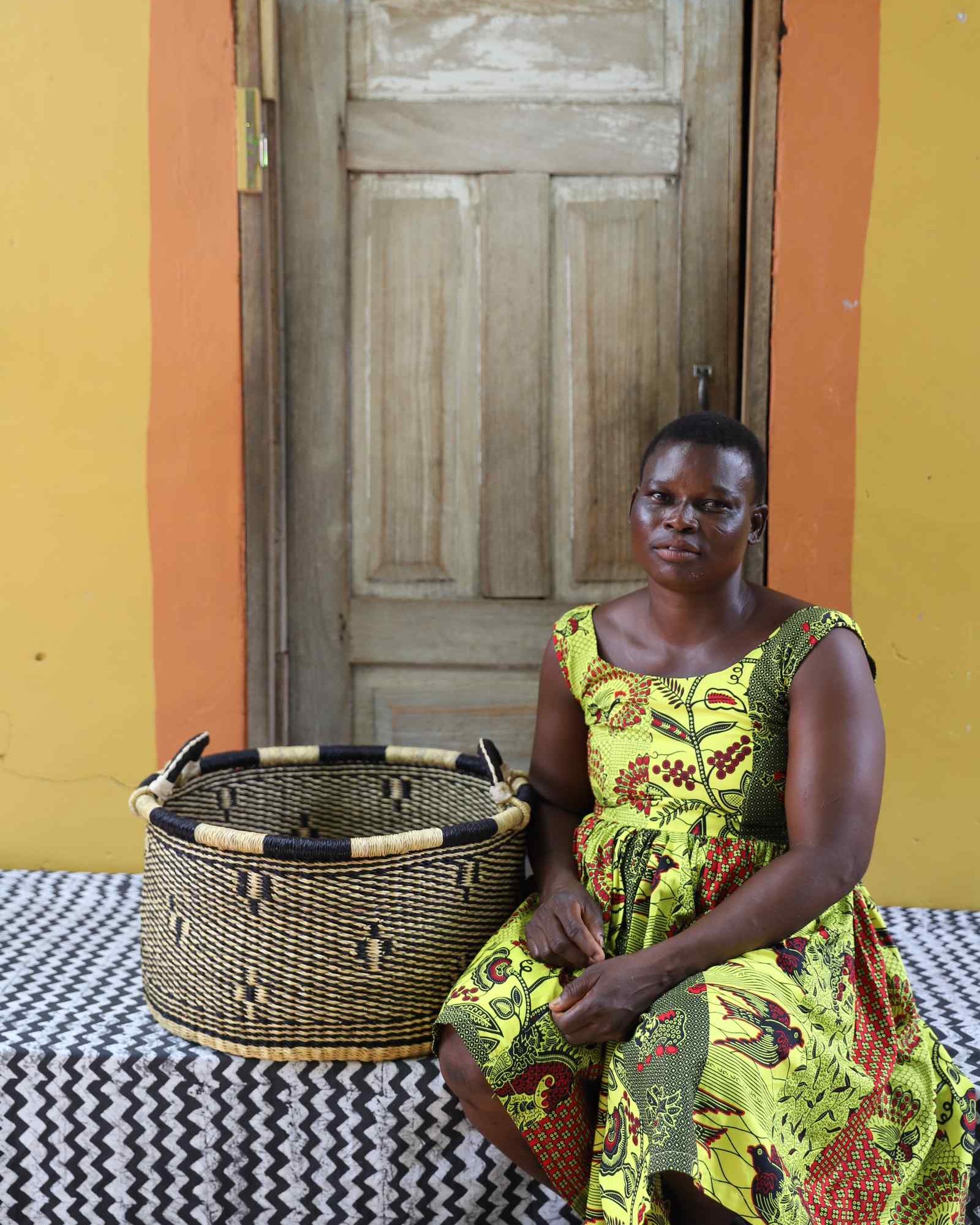 Handwoven Bolga storage basket in natural straw with a dark motif and banded rim, styled beside a seated woman.