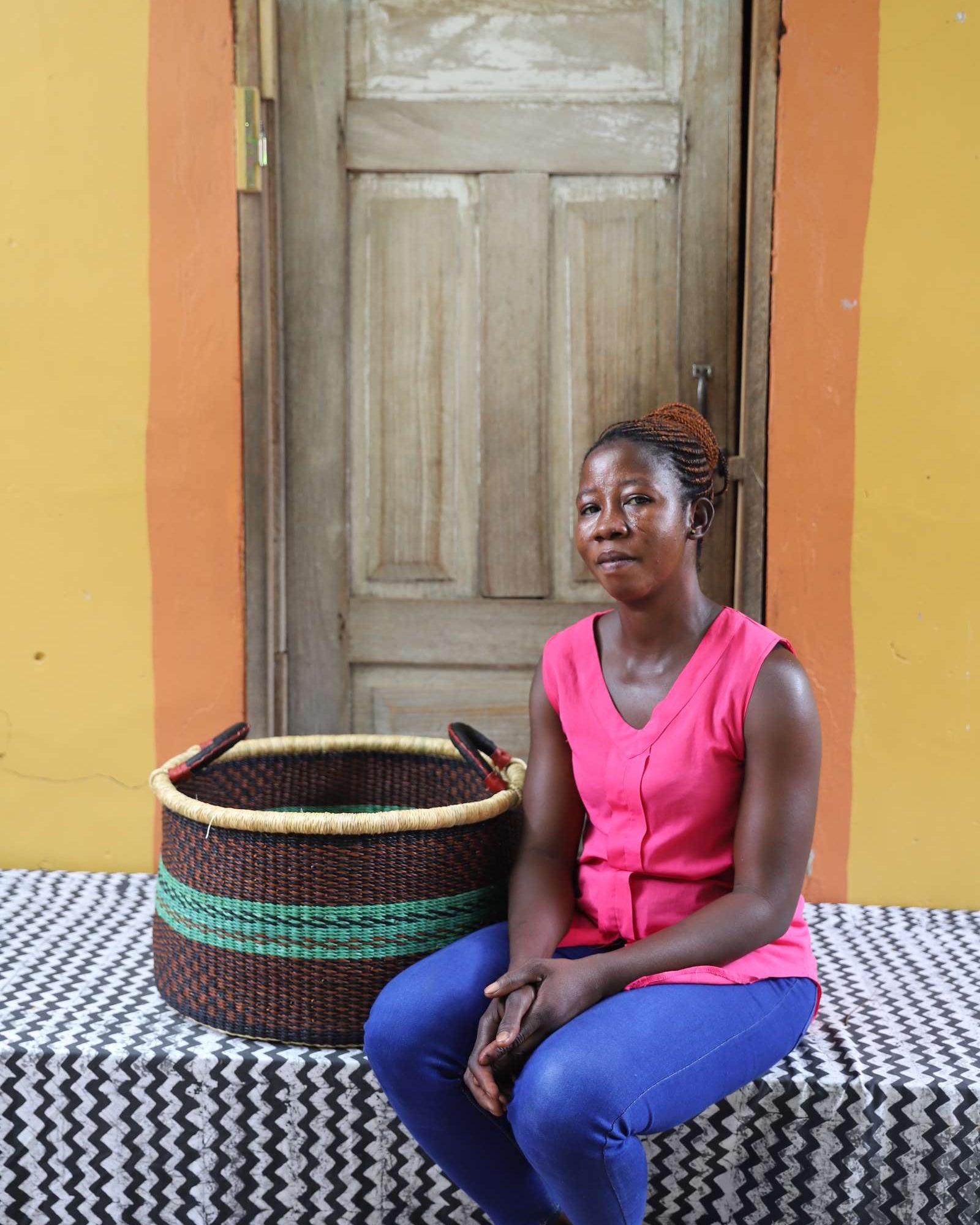 Handwoven Bolga storage basket in dark brown with green stripes, styled beside a seated woman in pink.