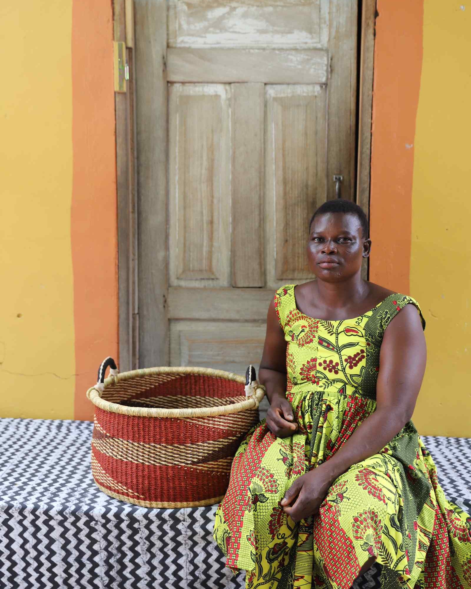 Handwoven Bolga storage basket in natural straw with red horizontal stripes, styled beside a seated woman.