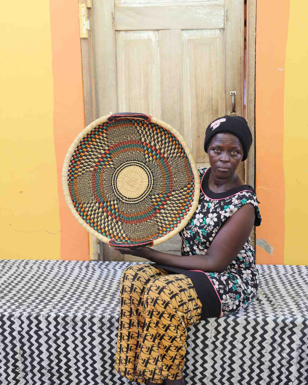 Handwoven Bolga wall tray disc with fine dark concentric bands, held by a seated woman in floral.