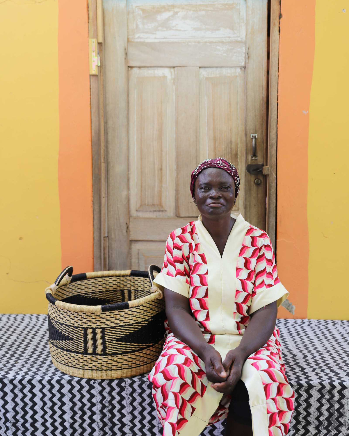 Small handwoven Bolga storage tub in black with natural stripes, beside a seated woman in red and white.