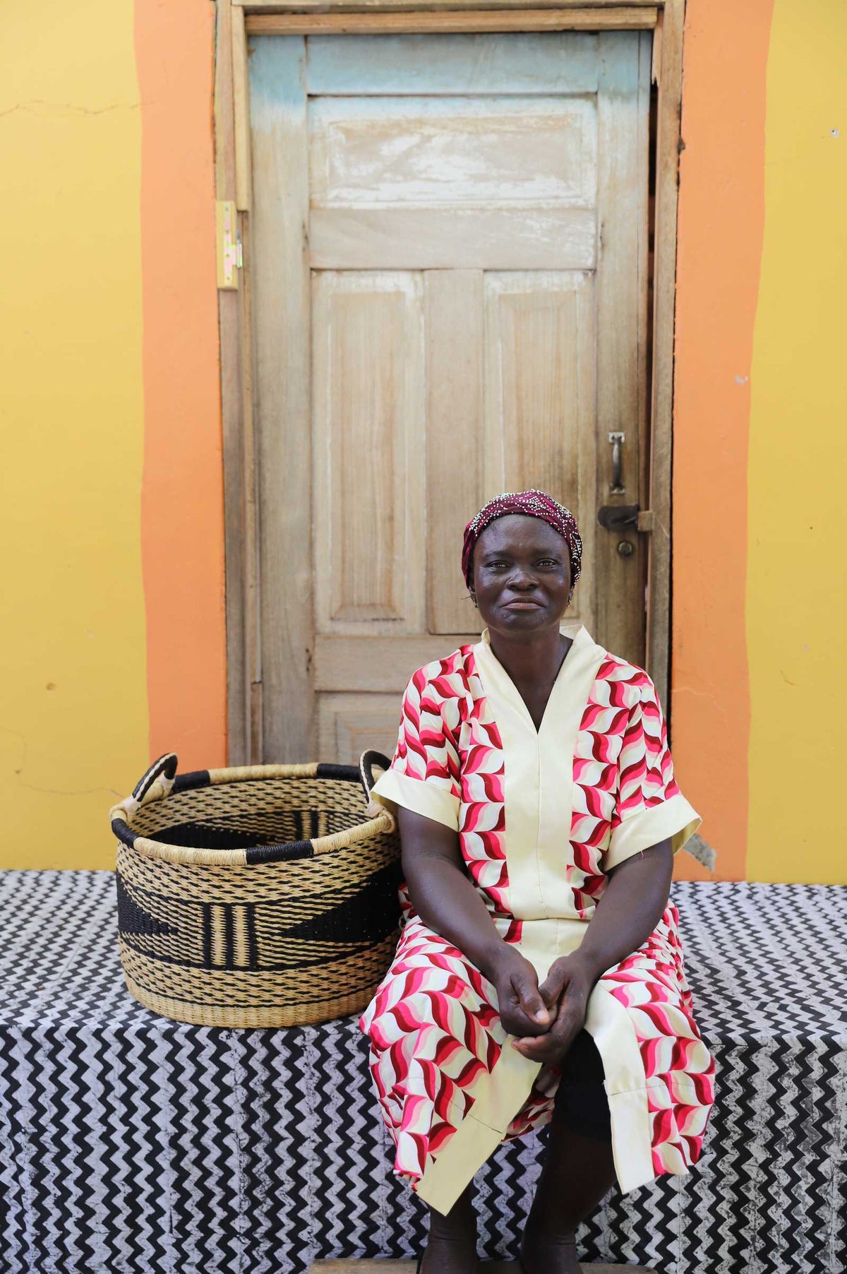 Small handwoven Bolga storage tub in black with natural stripes, beside a seated woman in red and white.