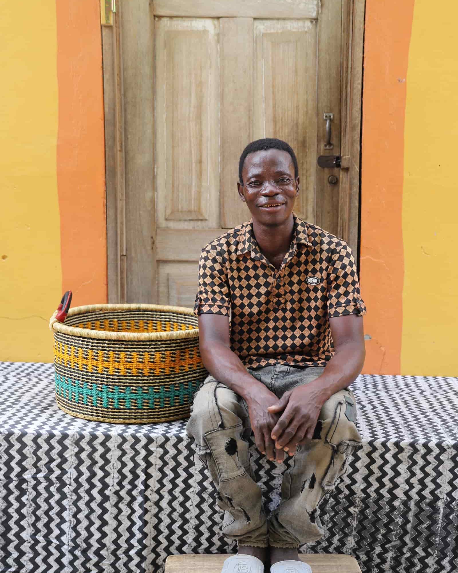 Woven Tub (Small) with man weaver handwoven in Ghana sitting on black and white cloth and wooden door in background