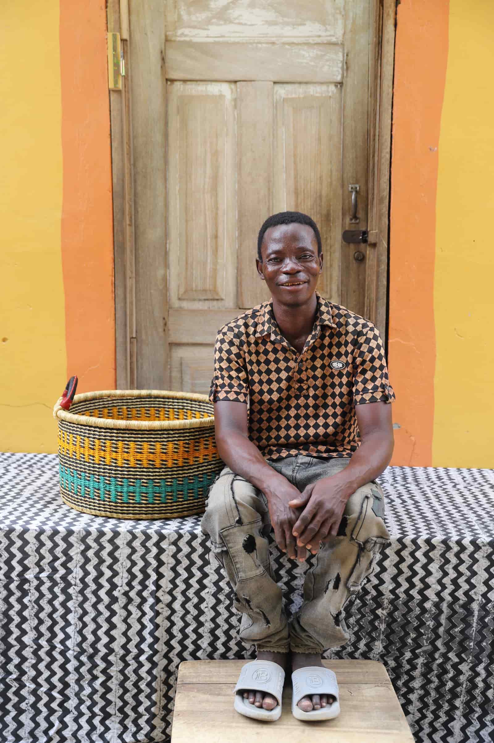 Woven Tub (Small) with man weaver handwoven in Ghana sitting on black and white cloth and wooden door in background
