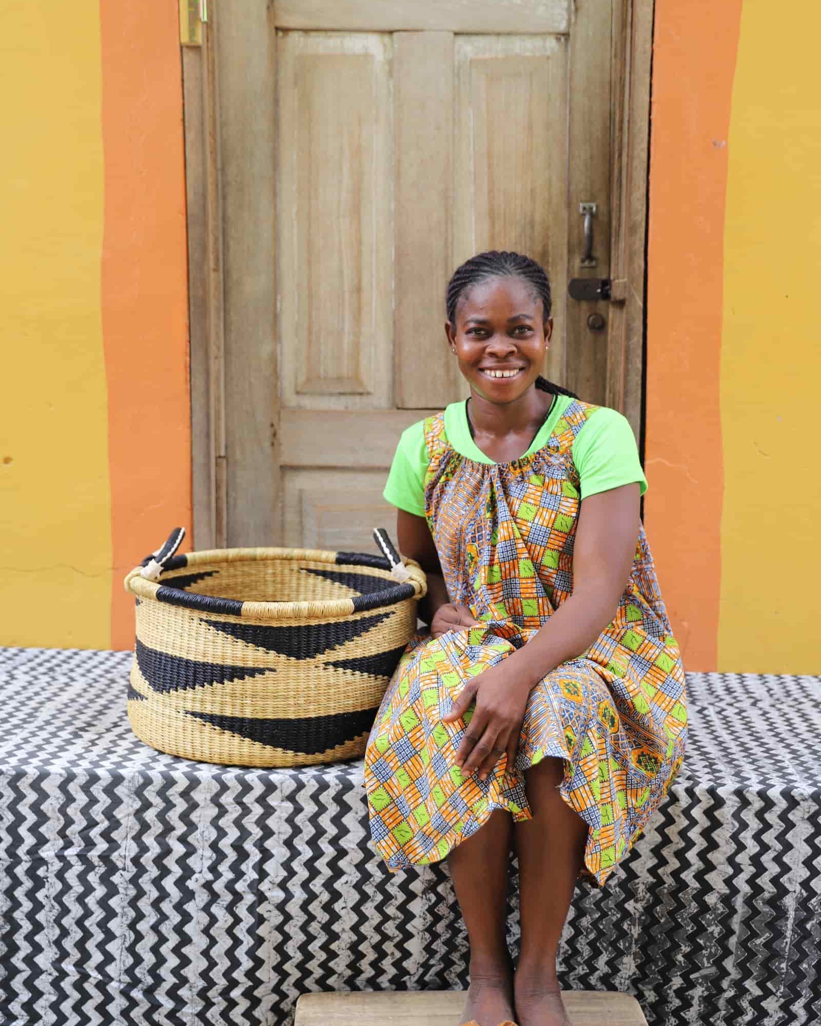 Woven Tub (Small) with woman weaver handwoven in Ghana sitting on black and white cloth and wooden door in background