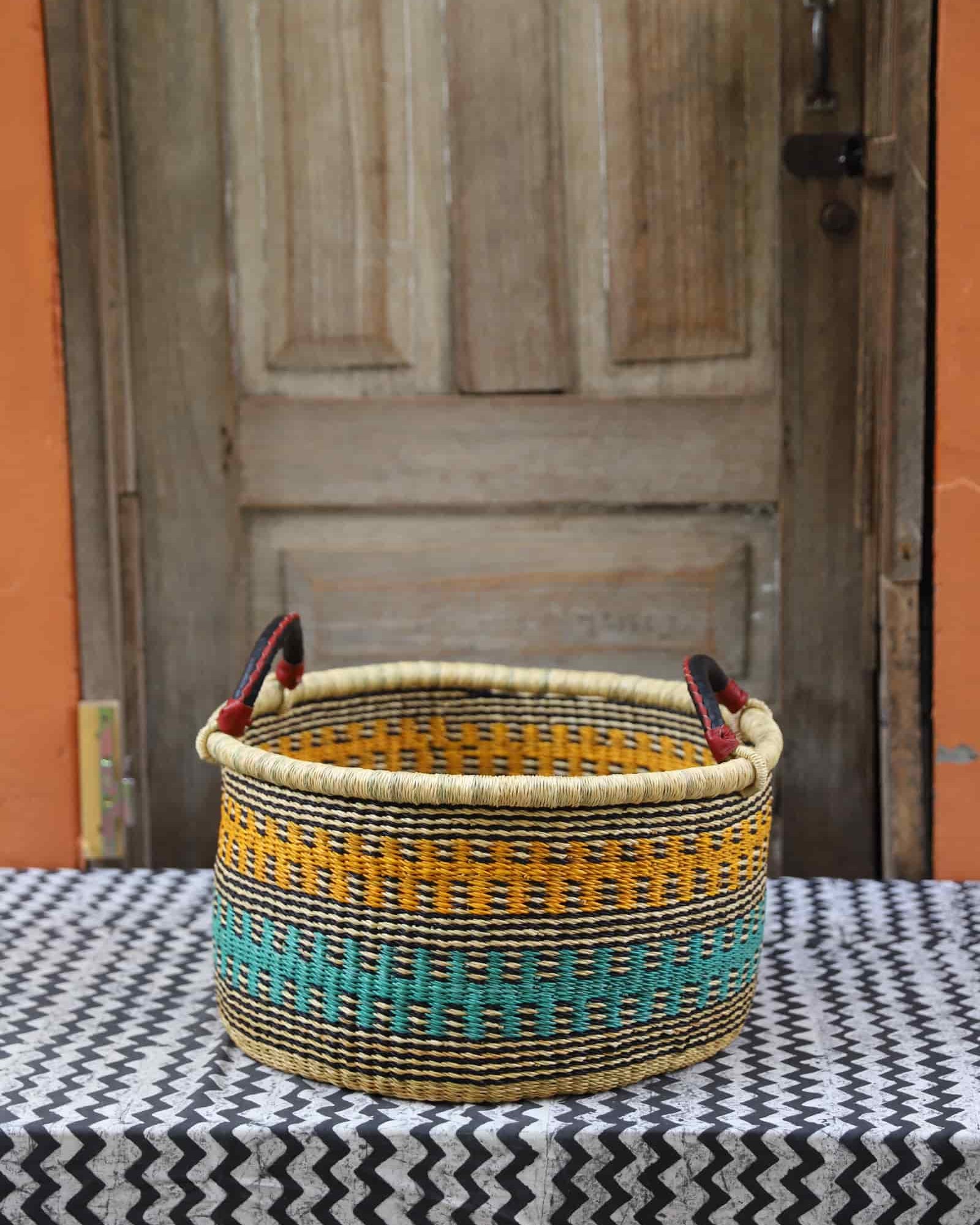 Woven Tub (Small) handwoven in Ghana sitting on black and white cloth with wooden door backgroundl) Handwoven in Ghana