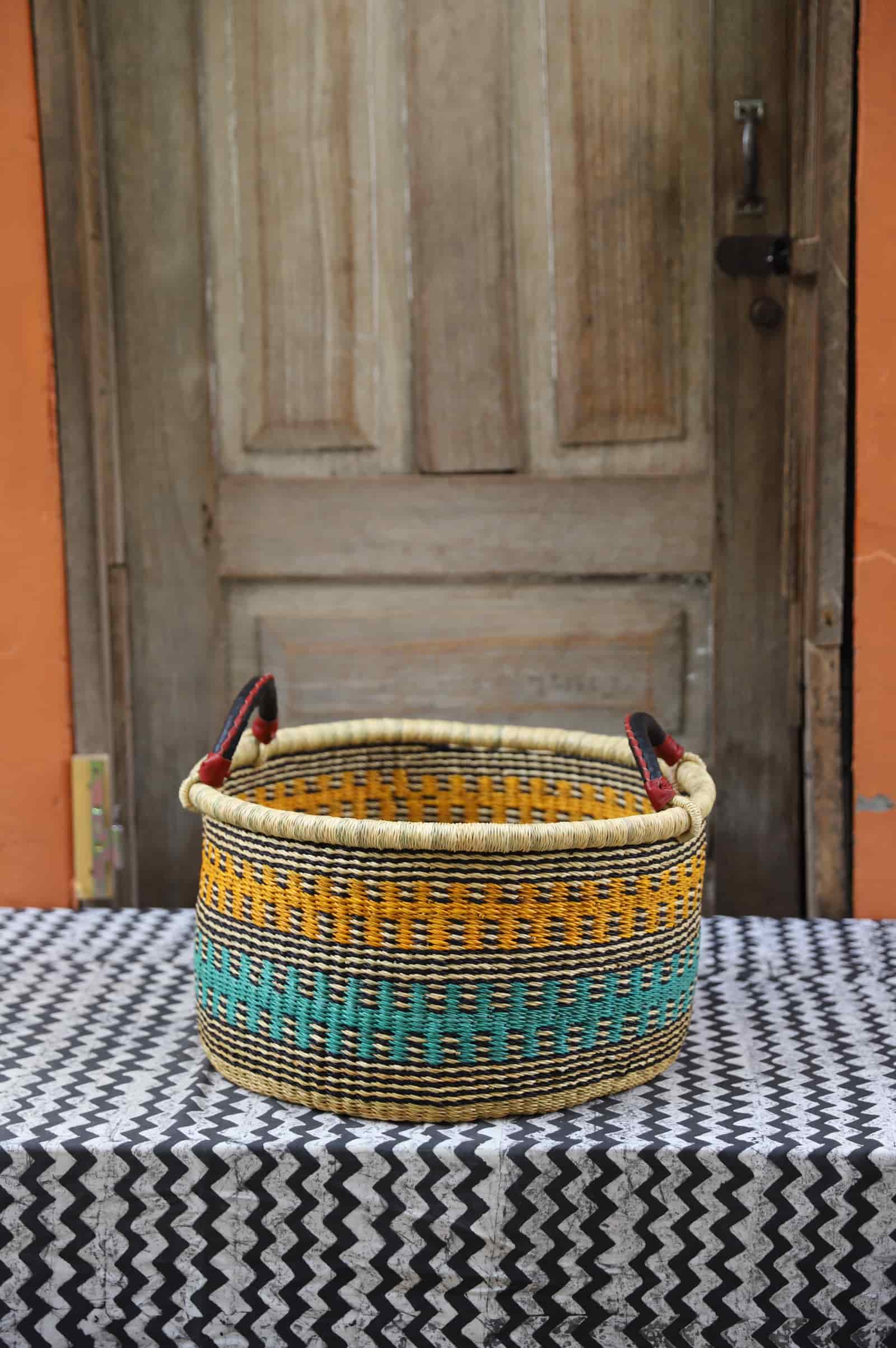 Woven Tub (Small) handwoven in Ghana sitting on black and white cloth with wooden door backgroundl) Handwoven in Ghana