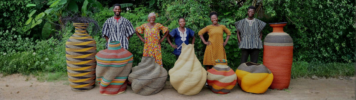 Five people smiling behind a row of large sculptural Bolga floor baskets and vases outdoors.