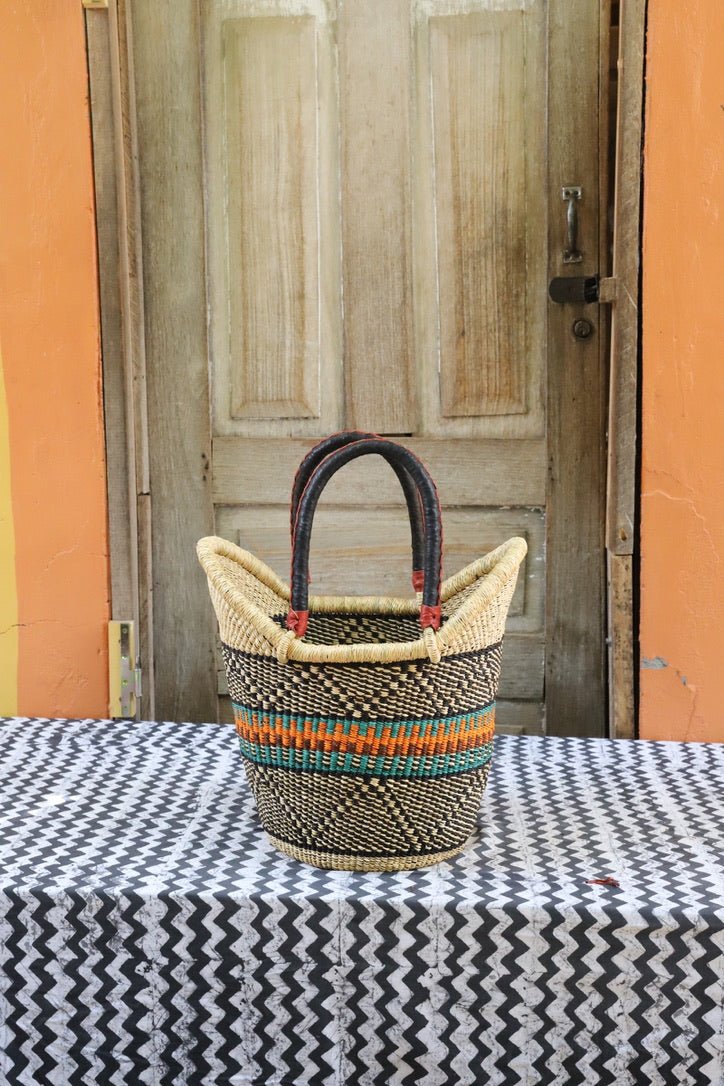 Woven basket with colorful handles on a tablecloth in front of a wooden door.