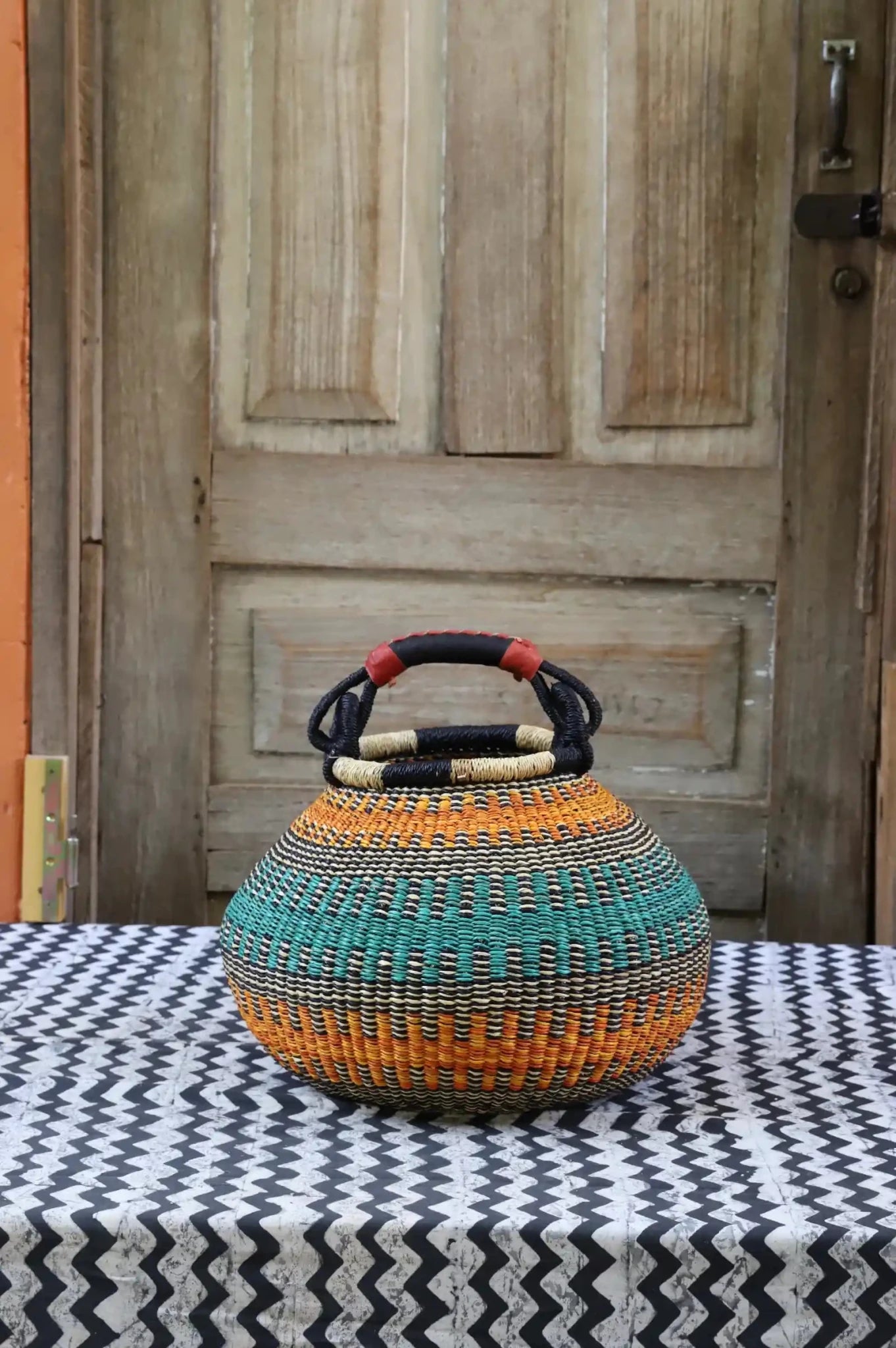 Colourful storage basket sitting on a black and white cloth against a wooden door.