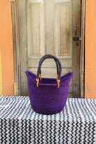 Purple woven basket with black handle on a table in front of a wooden door.