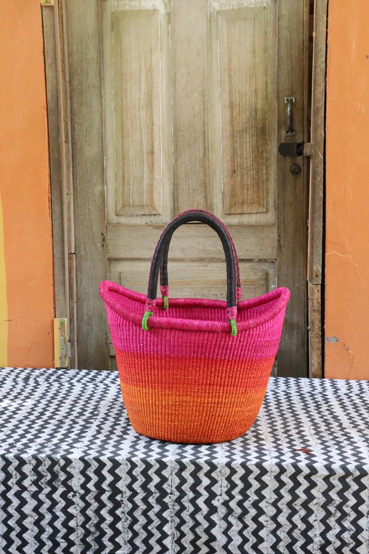 Woven basket with pink and orange gradient on a black and white patterned tablecloth, wooden door in the background.