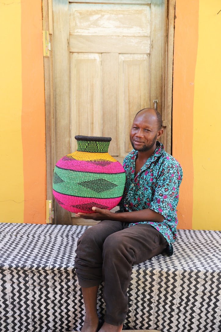Artisan holding a colorful woven storage basket  on a black and white cloth against a wooden door.