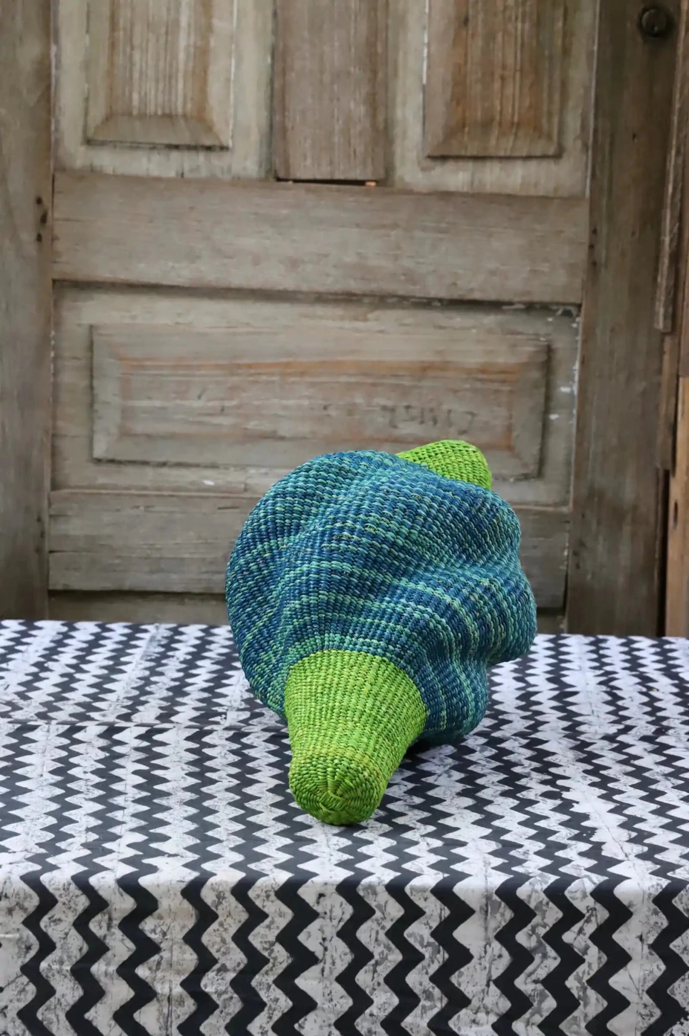 Woven conch piece on a black and white patterned surface with a wooden door in the background.