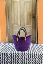 Purple woven basket with black handles on a table in front of a wooden door.