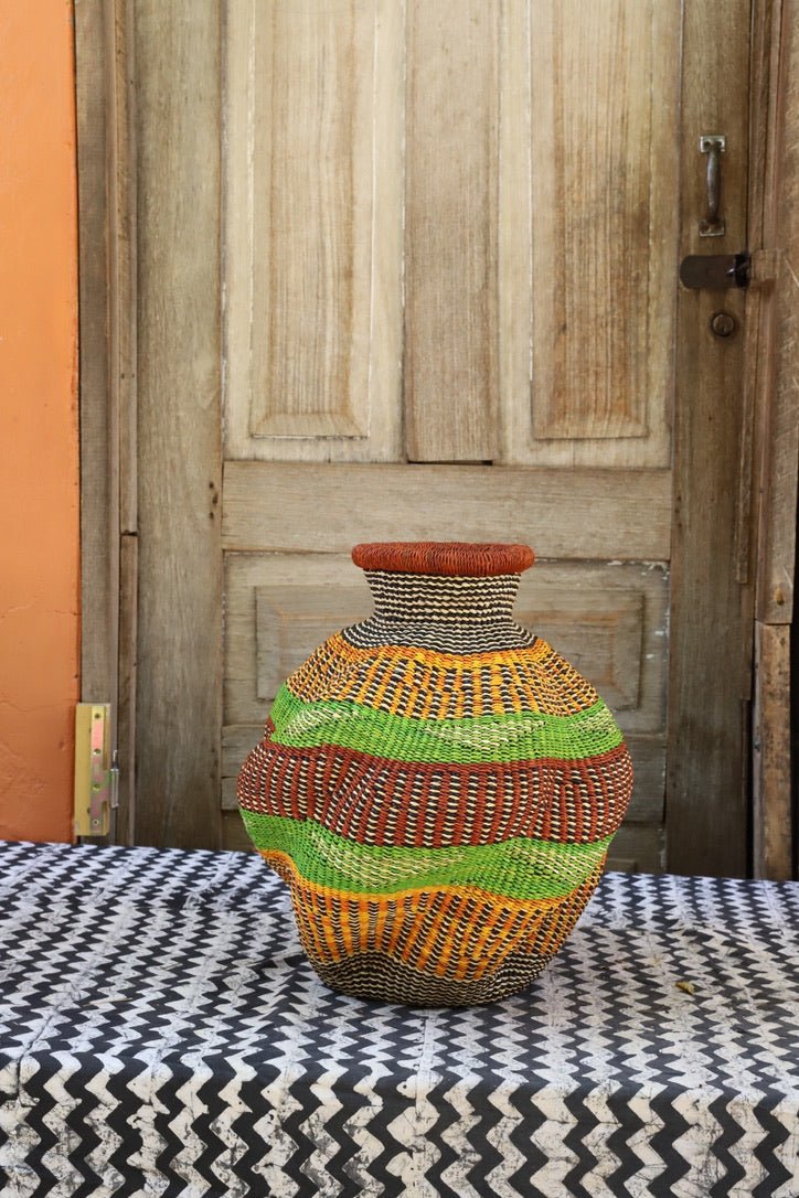 Colorful woven piece on a black and white patterned surface with a wooden door in the background.