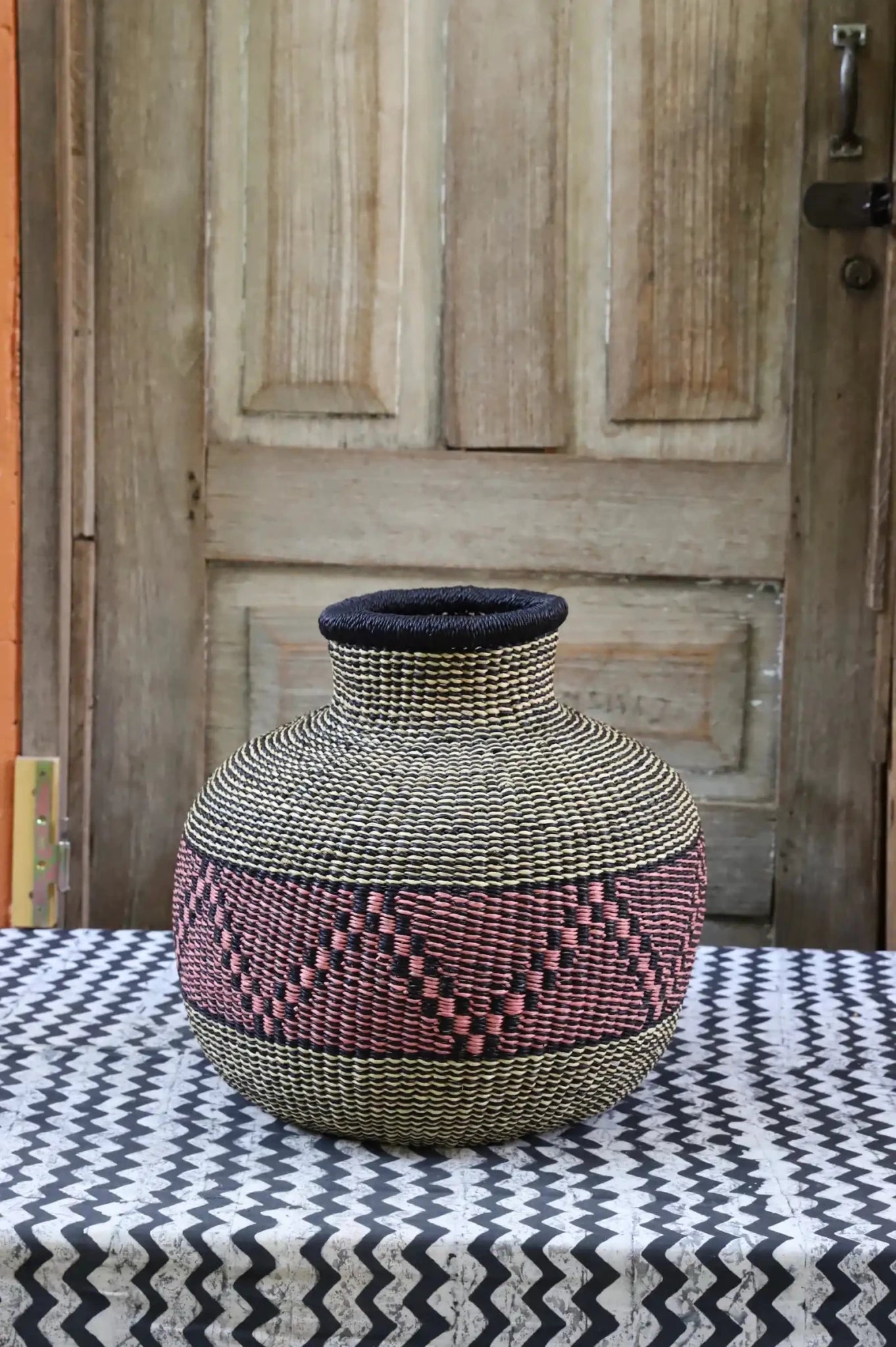 Decorative handwoven basket with colorful patterns on a black and white cloth against a wooden door.