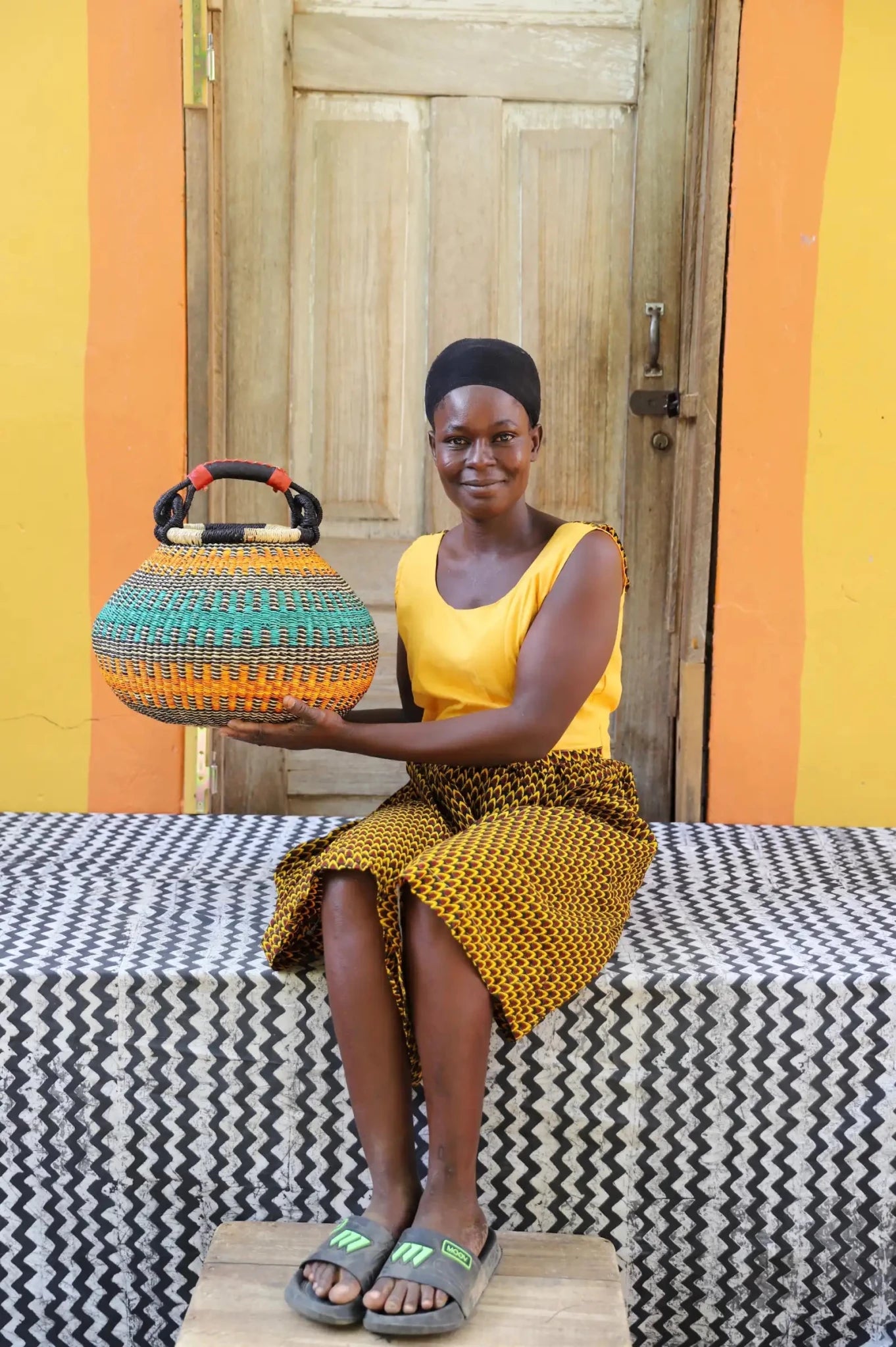 Small pot storage basket in yellow, teal and gold, being held up to show the shape
