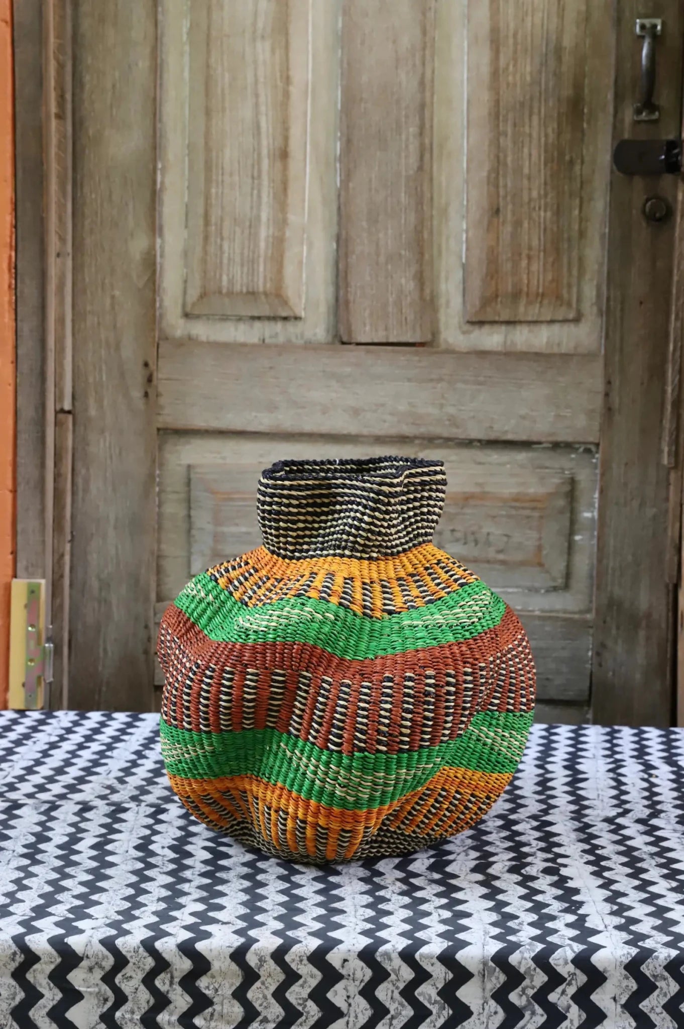 A colorful, handwoven piece with decorative curves sitting on a black and white cloth against a wooden door