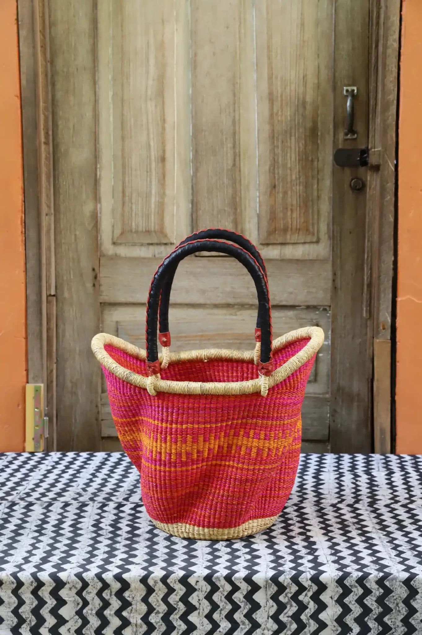 Woven carry on basket with premium leather on a black and white cloth against a wooden door