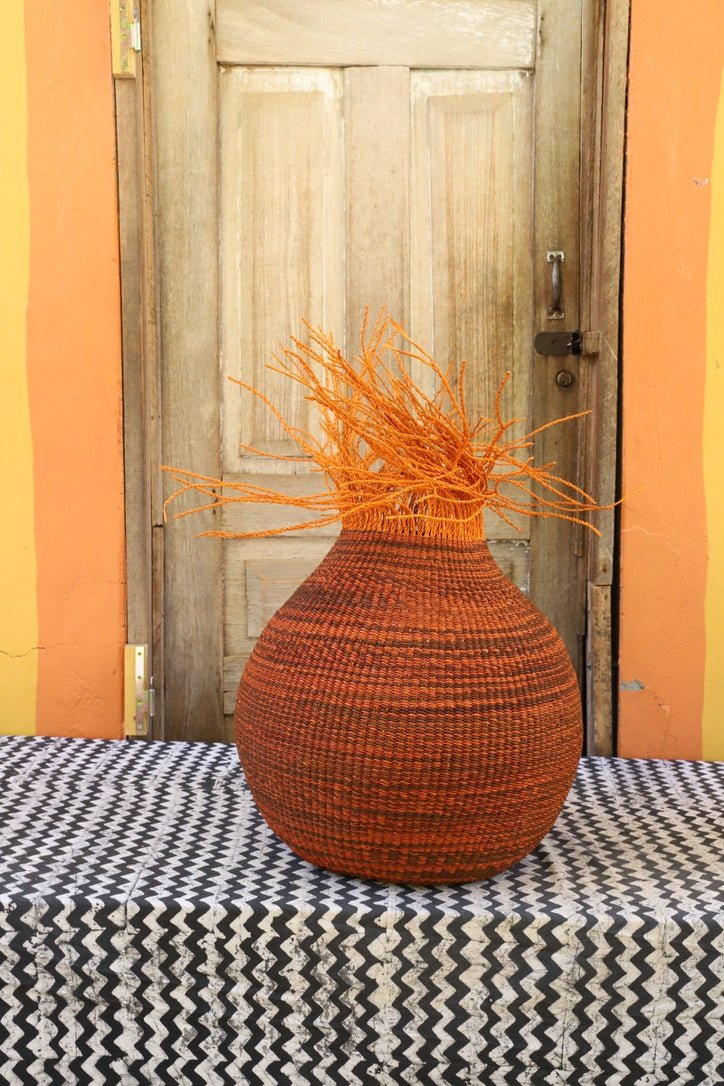 Colorful woven décor basket with straw branching out on a black and white cloth with a wooden door in the background.