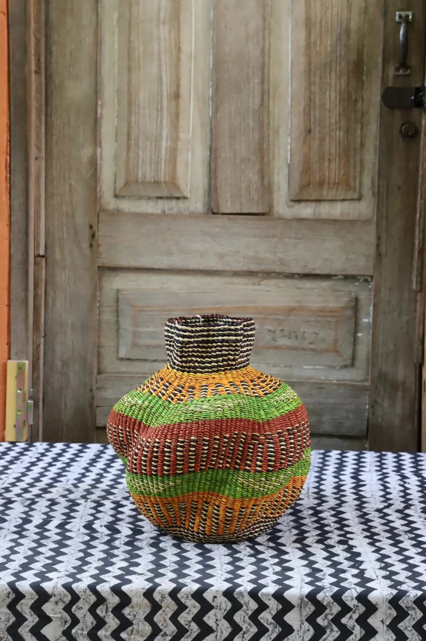 A colorful, handwoven piece with decorative curves sitting on a black and white cloth against a wooden door