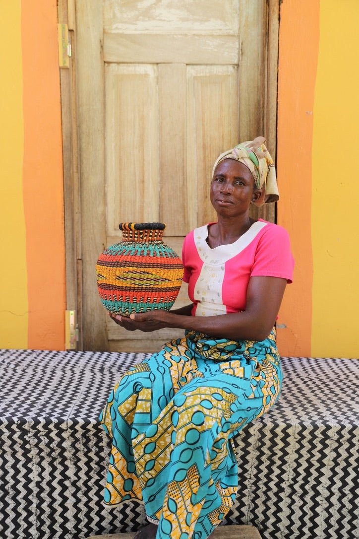 Artisan holding a colorful woven storage basket  on a black and white cloth against a wooden door.