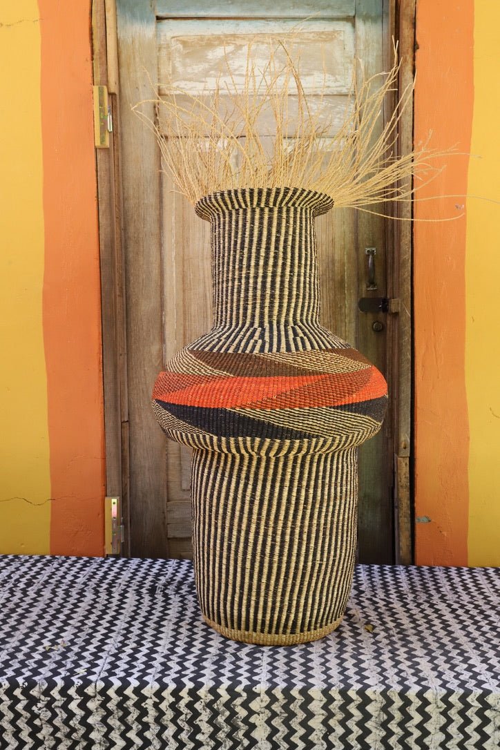 Colorful woven basket with stylish branches on a black and white patterned surface with a wooden door in the background.