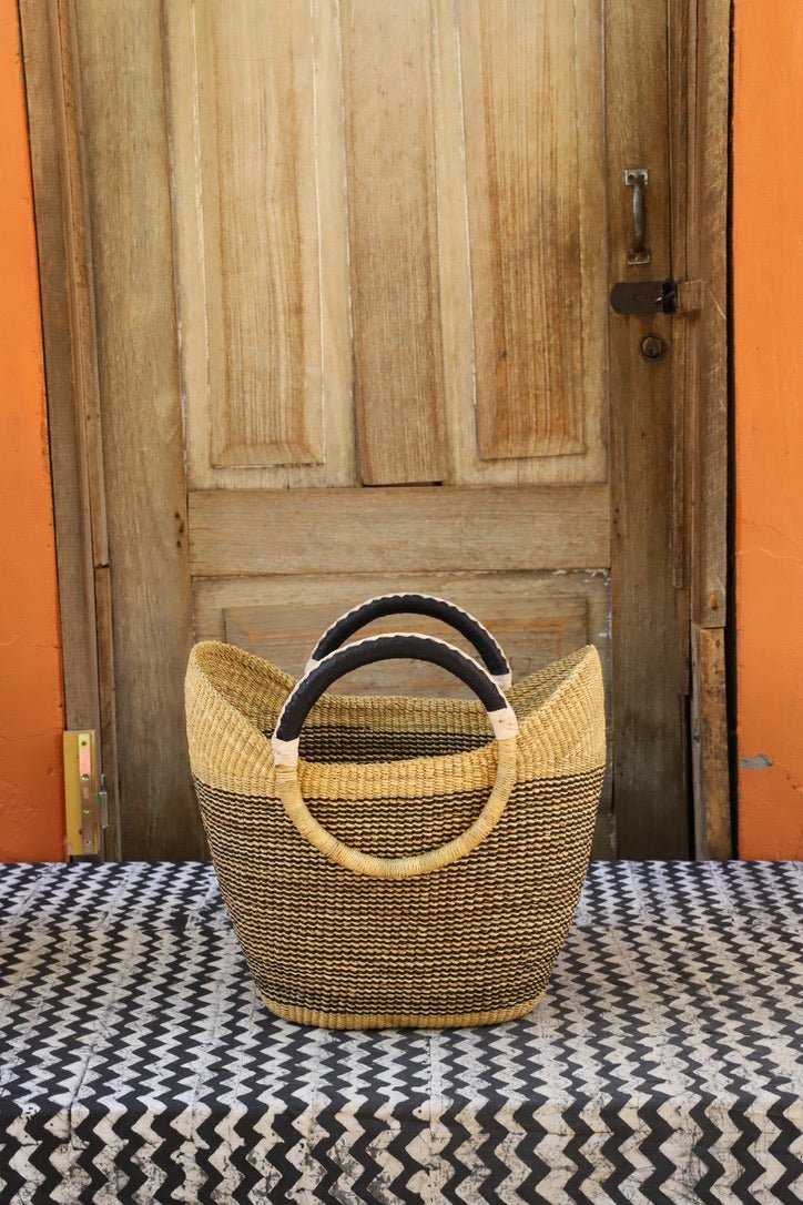 Woven carry on basket with premium leather on a black and white cloth against a wooden door