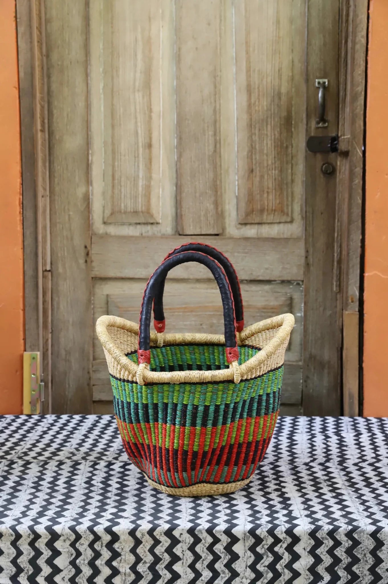 Woven carry on basket with premium leather on a black and white cloth against a wooden door