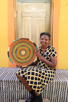 Woman holding a colorful woven basket against a yellow wall.